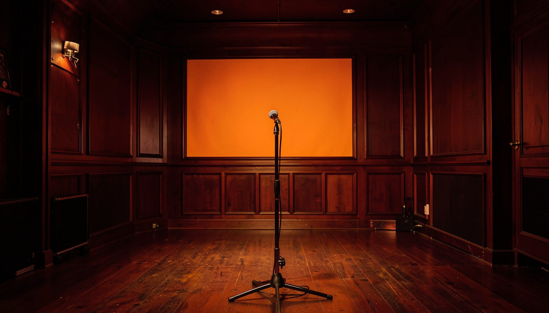 Warmly lit jazz club interior with a stage, microphone stand, and deep amber and burgundy tones against dark wood paneling
