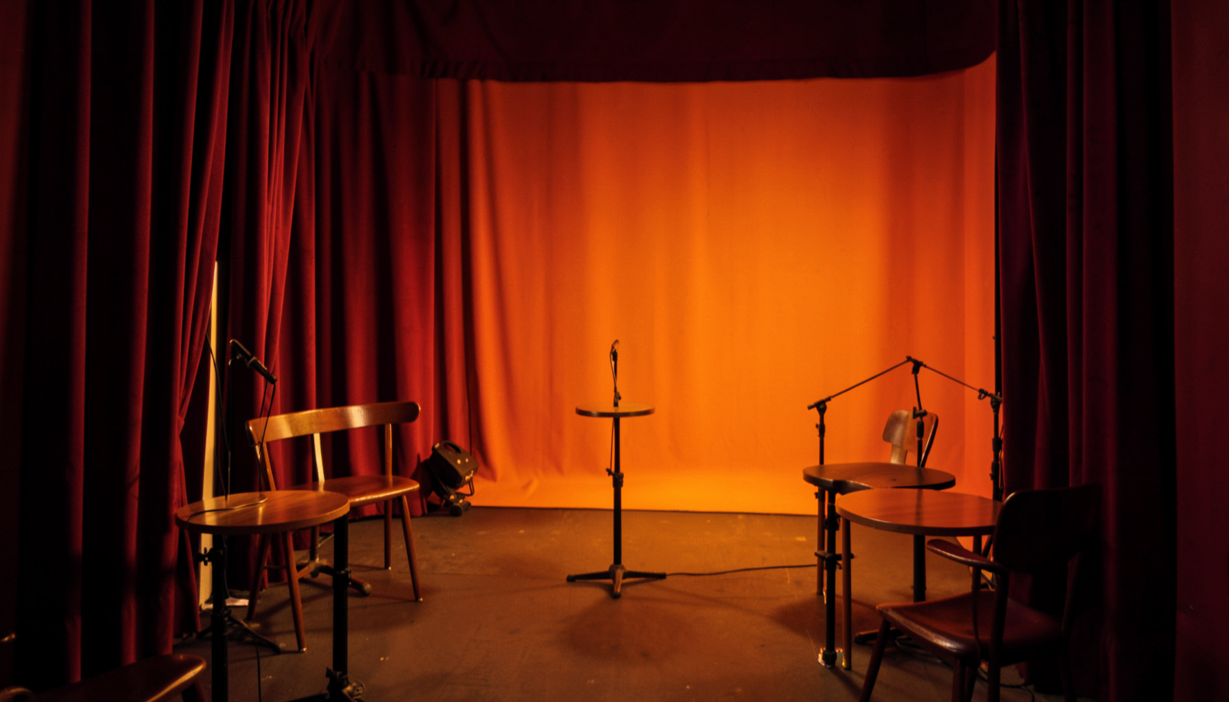 Intimate jazz performance space with warm amber lighting, small round tables, and a stage area framed by deep red curtains