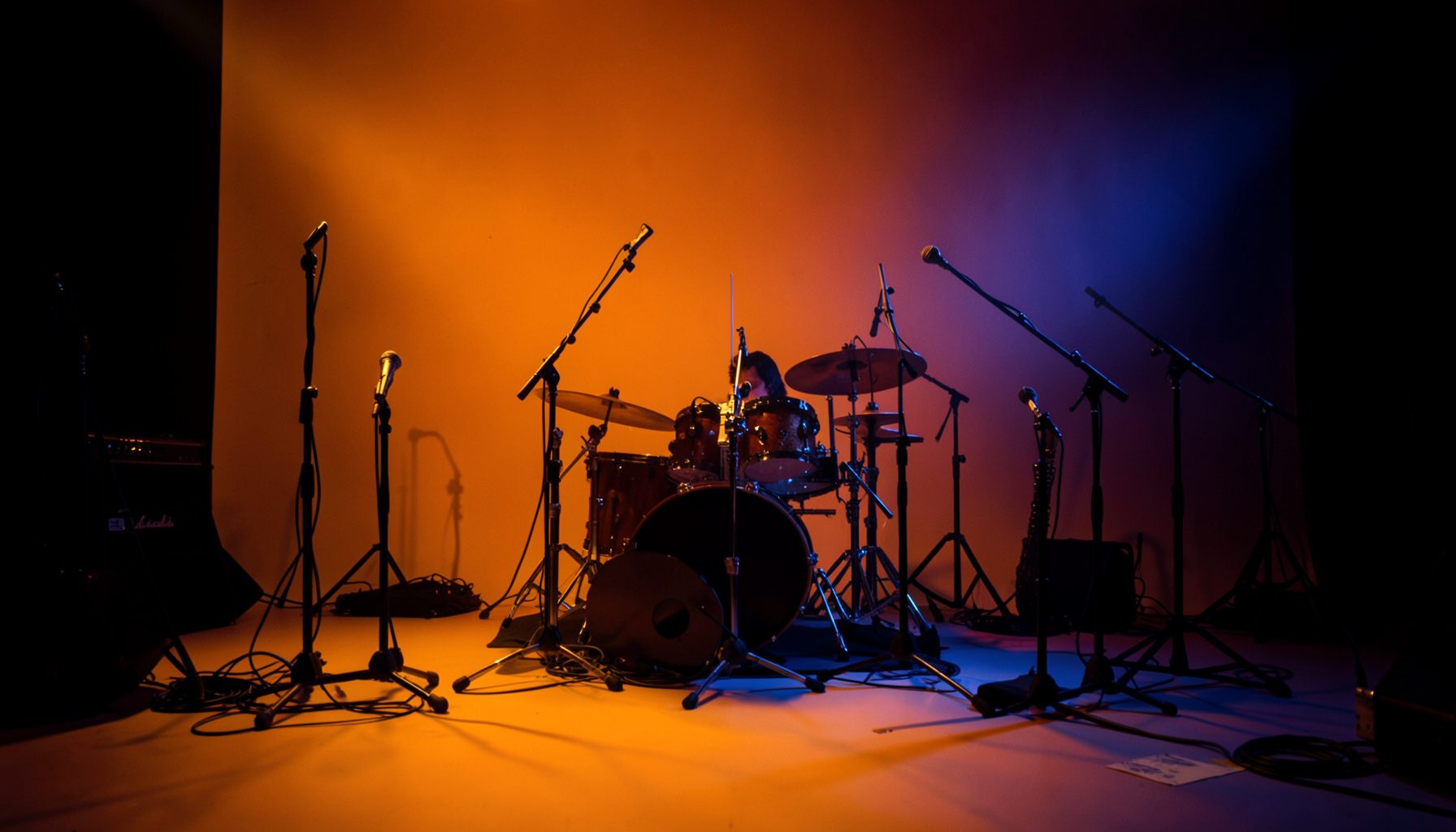 Warm stage lighting casting amber and deep blue tones across a jazz performance space, with microphone stands and instruments silhouetted against a dark backdrop