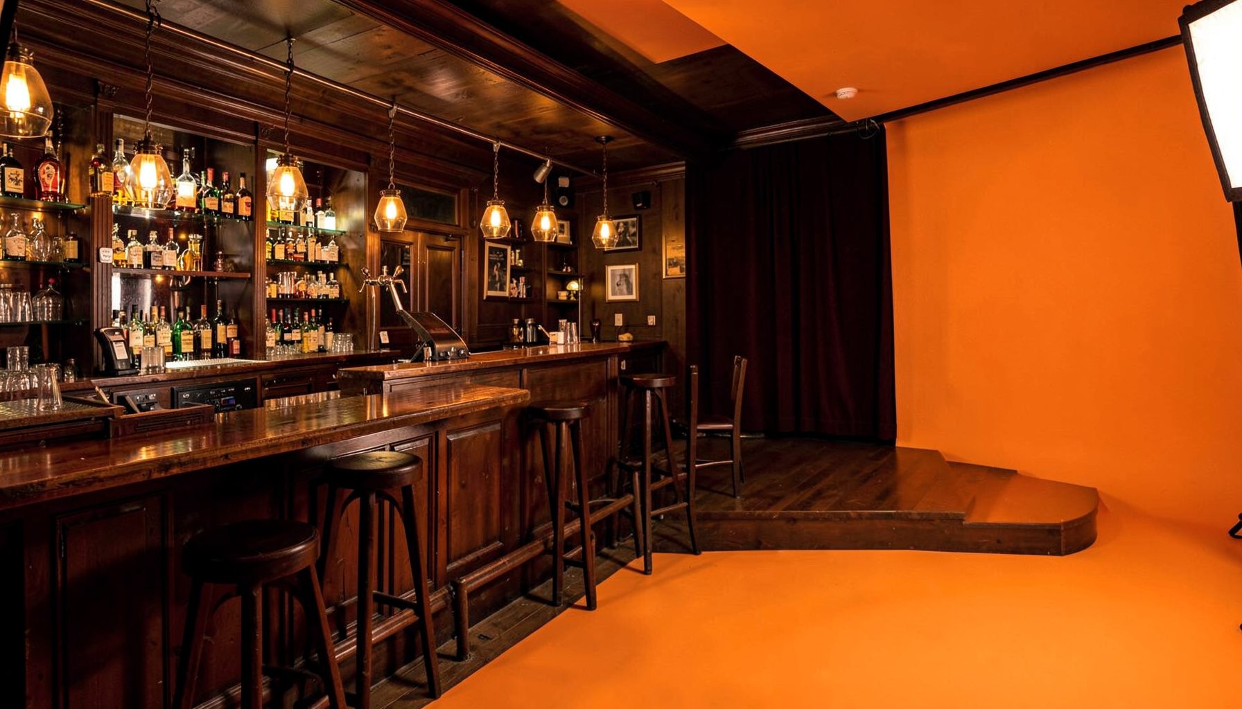 Warm pub interior with wooden bar, amber lighting, and a raised stage area, cozy and inviting