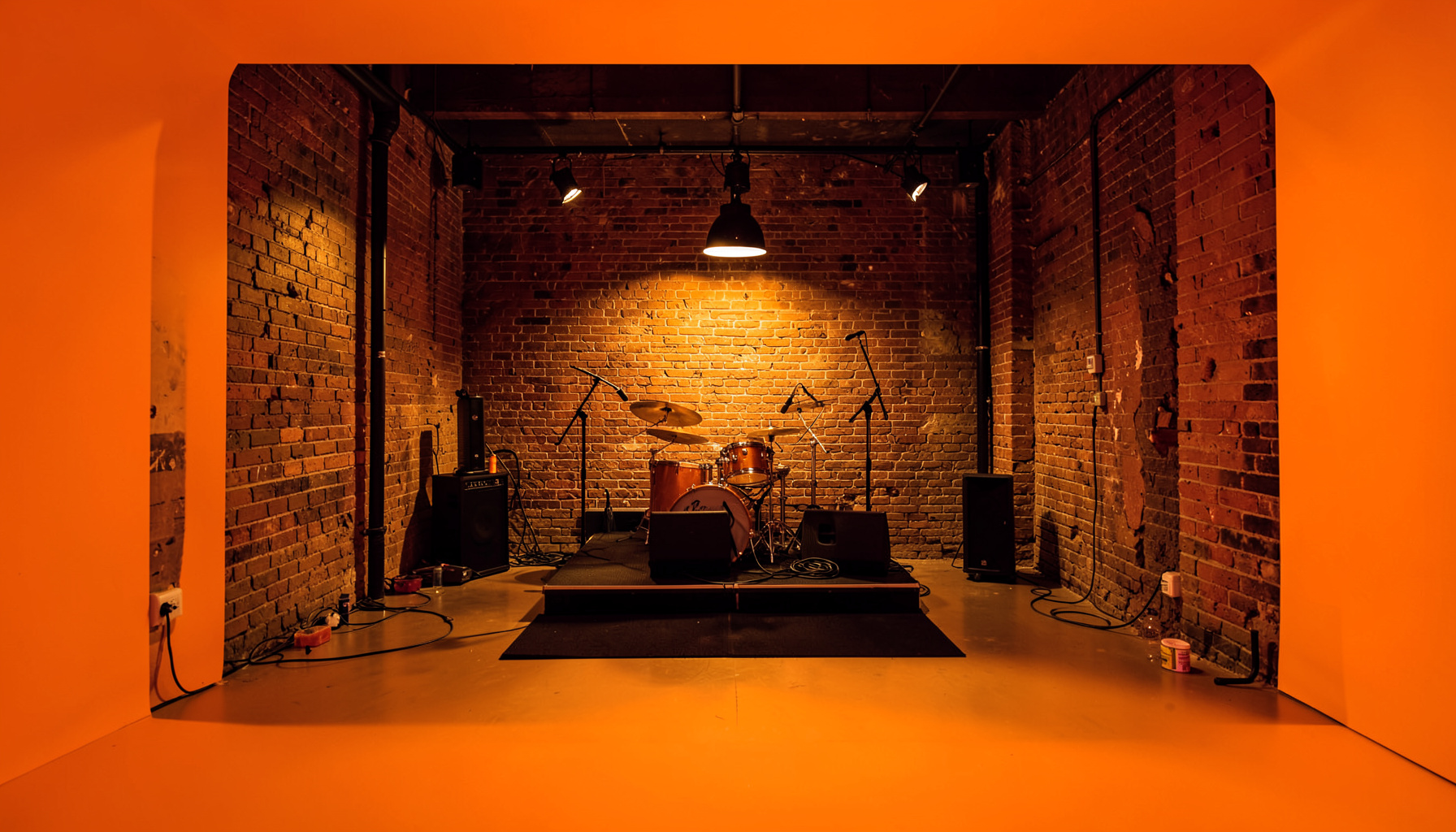 Warmly lit interior of a music venue with exposed brick walls and a small stage, amber and deep brown tones, intimate jazz-club atmosphere