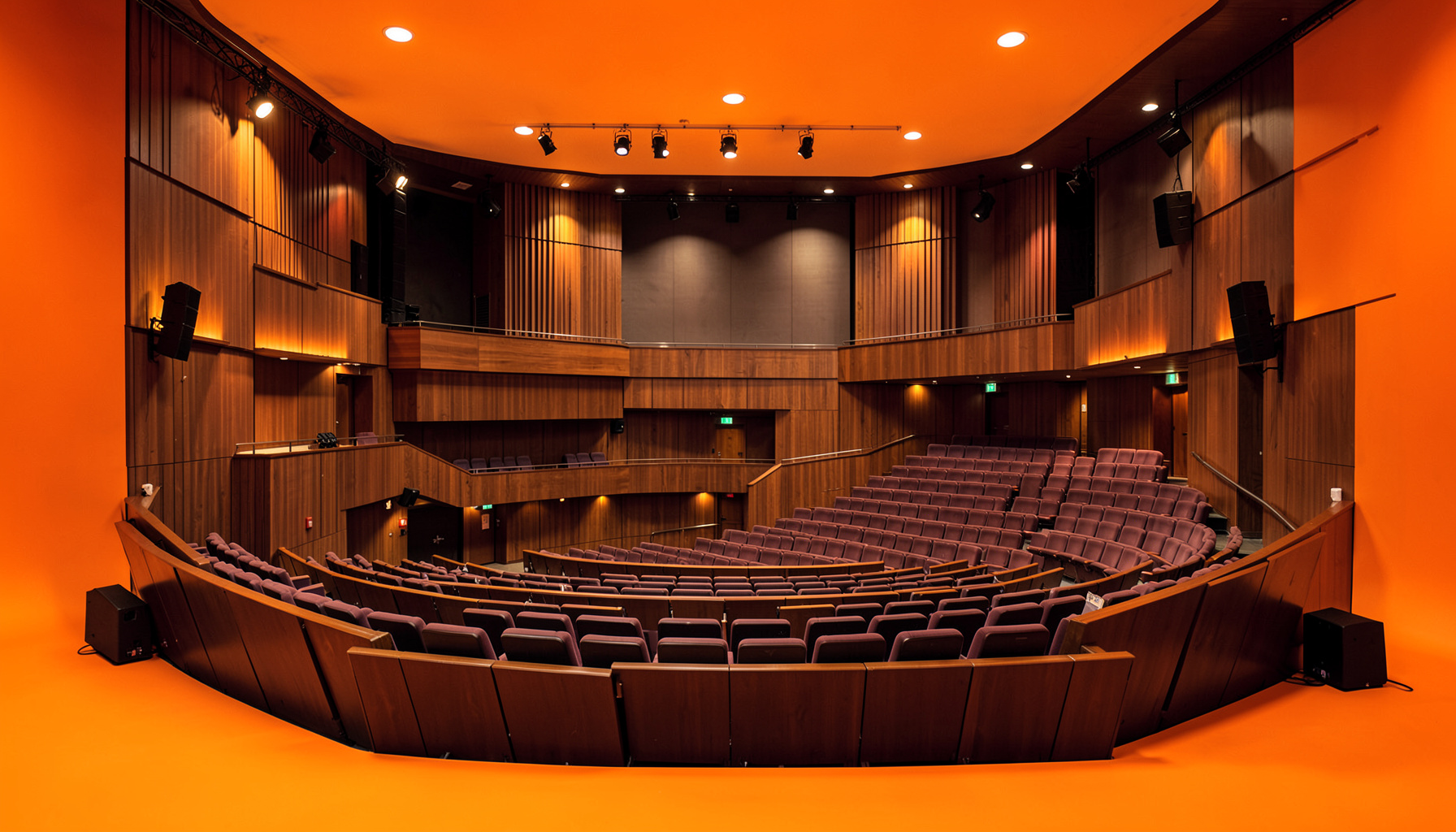 Contemporary theatre auditorium with raked seating, warm wood panelling, and stage lighting