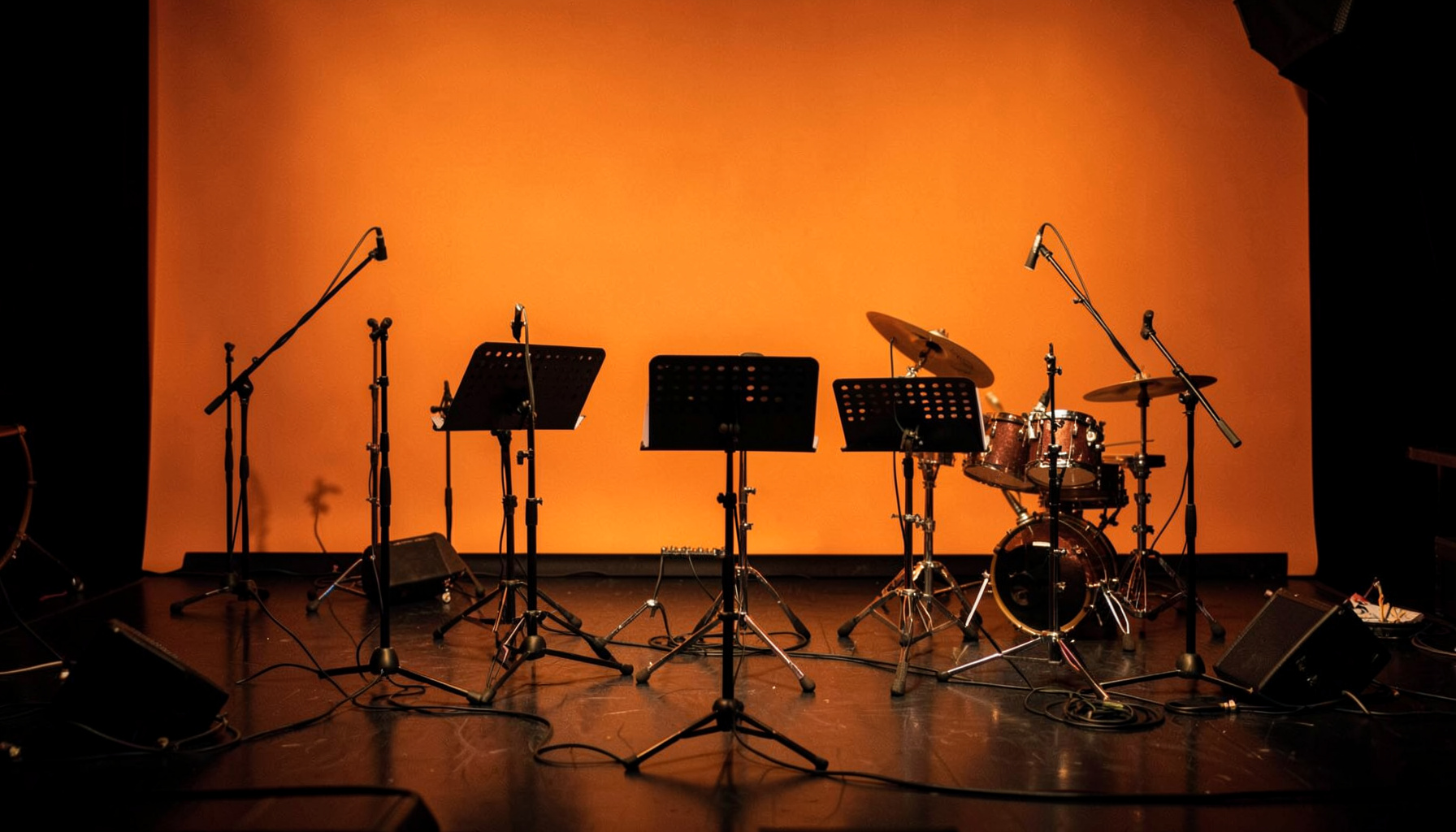 Warmly lit jazz workshop setting with music stands and instruments on a dark stage, rich amber and deep brown tones