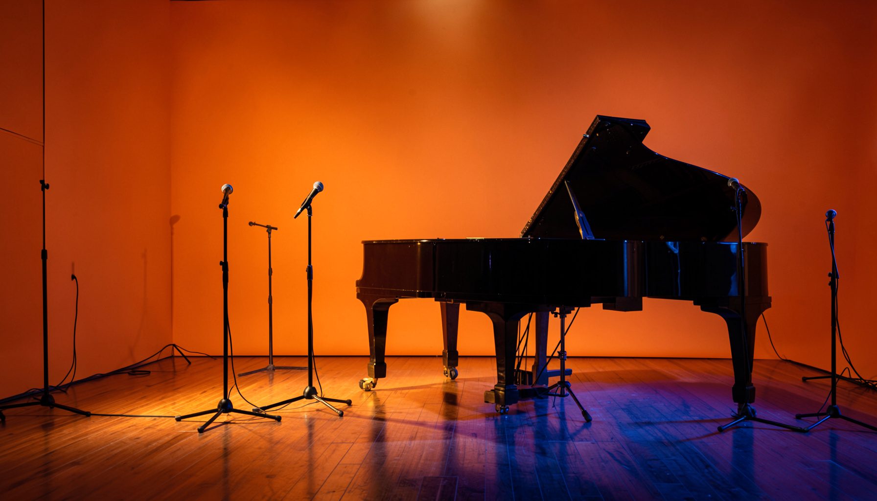 Warm stage lighting casting amber and deep blue tones across an empty jazz club interior with microphone stands and a grand piano on a polished wooden floor